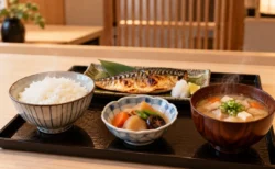 木のカウンターに並ぶ炊きたての白いご飯と味噌汁、焼き魚の和食膳