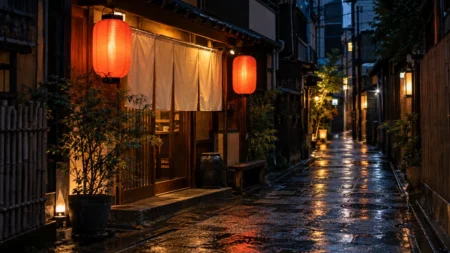 夜の路地裏に赤い提灯と白い暖簾がともる小さな和風の食堂と、雨に濡れた石畳
