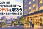 2026年11月 Stray Kids東京ドームのホテルを取ろう。徒歩圏と電車で帰れる5選。ホテル前を歩く旅行者のイラスト。