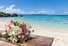 遠浅の青い海と白い砂浜を背景に木のテーブルに置かれた花束