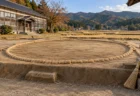秋の田園と山並みを背景に、古い木造校舎の前に設けられた屋外の土俵