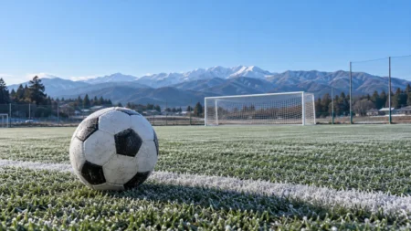 冬の高校のサッカーグラウンド、ゴール前に置かれたサッカーボールと遠くの雪をかぶった山並み