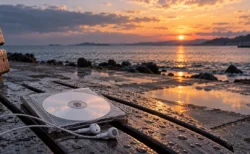 雨上がりの夕方の海辺に置かれたCDとワイヤレスイヤホン