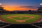 夕暮れの空の下で照明がともる無人の野球場のダイヤモンドと観客席