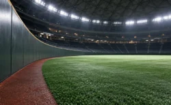 ナイター照明に照らされたドーム球場の、試合前の誰もいない外野グラウンドとフェンスのイメージ