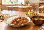 木のテーブルに並んだ湯気の立つ家庭料理と取り皿